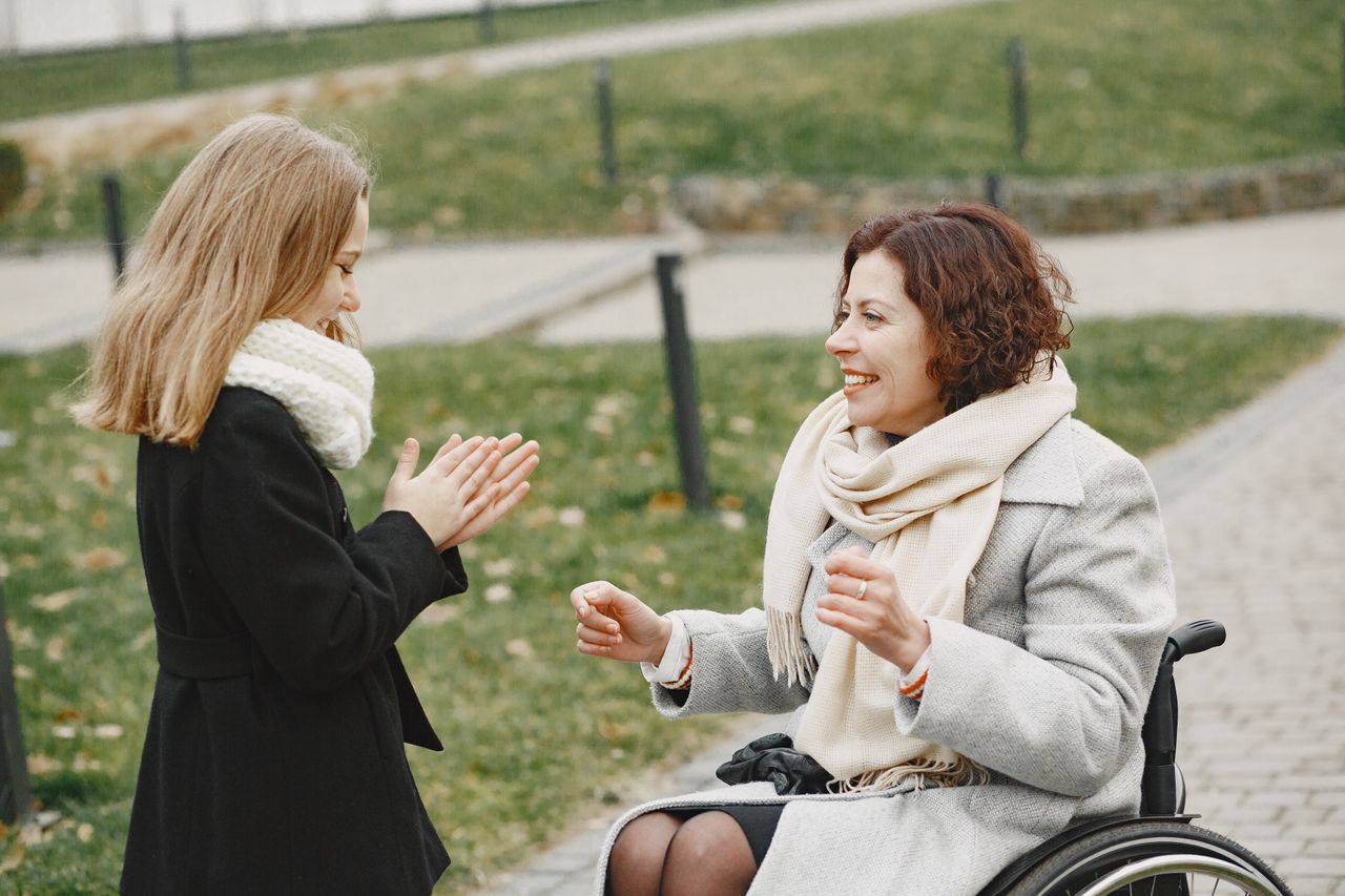 A woman in a wheelchair and a child enjoy a playful outdoor moment, smiling warmly.