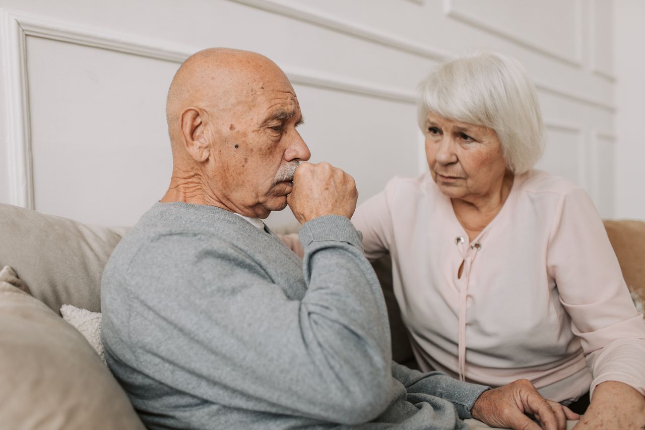An elderly couple sitting on a couch, showing care and affection indoors.